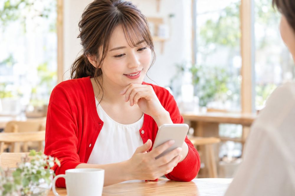 女性がカフェのテーブルで、スマホのメッセージ画面を見ながら相談している