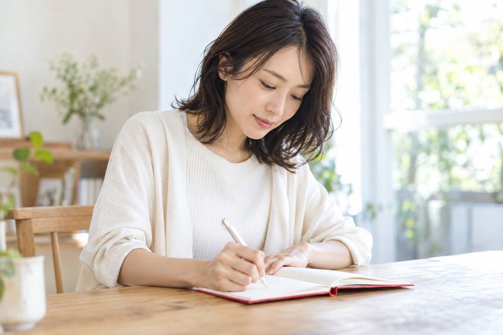 30代の女性が静かな部屋で、ノートに自分の気持ちと次にやることを書き出している