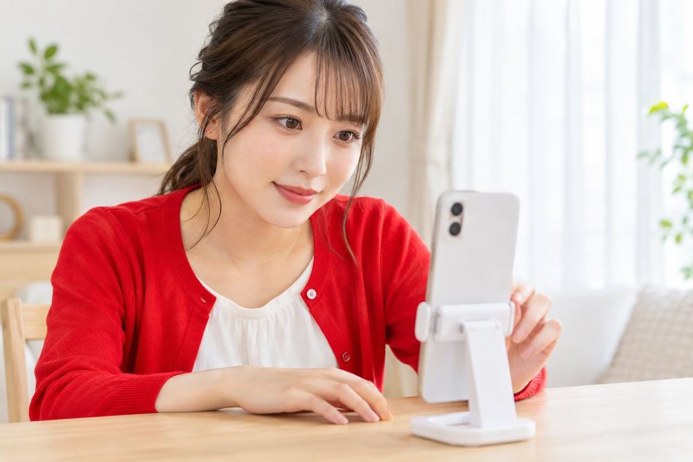 明るい部屋でスマホを立てかけ、配信画面の設定を確認している20代の女性