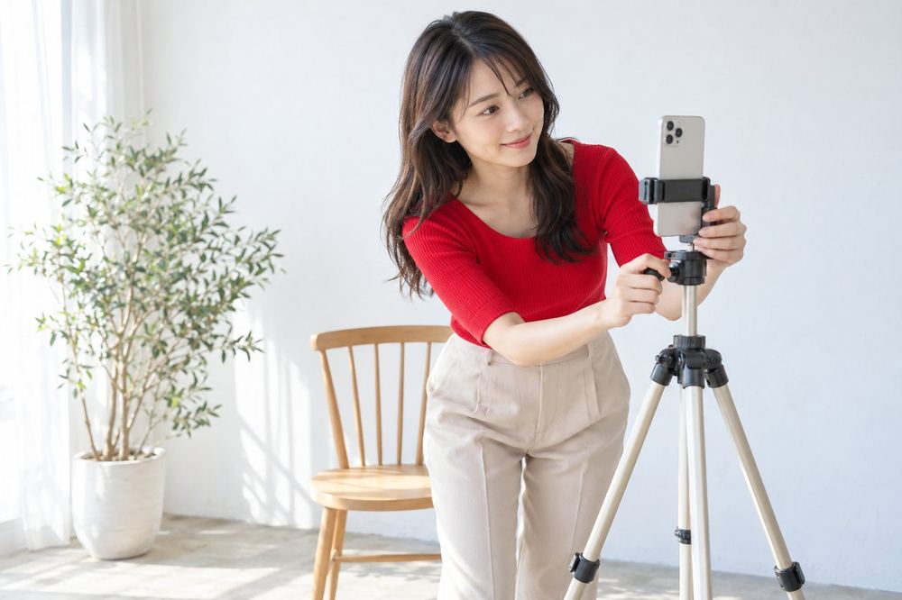 20代の女性が白い壁の前に椅子を置き、カメラの位置を変えながら一番きれいに映る場所を探している