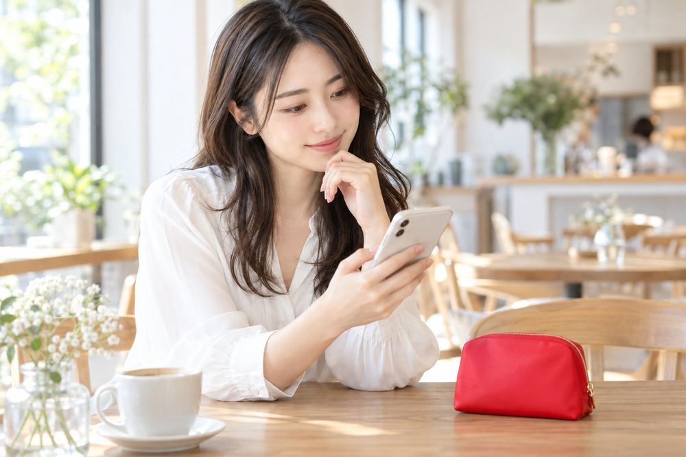 女性がカフェのテーブルでスマホのメッセージ画面を見ながら、メイクの相談内容を考えている