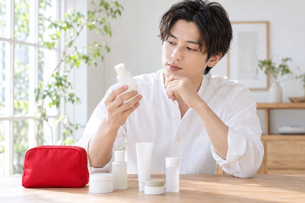 テーブルに小さな化粧品を並べた男性が、一つずつ手に取って、成分の表示と使い方を確かめている