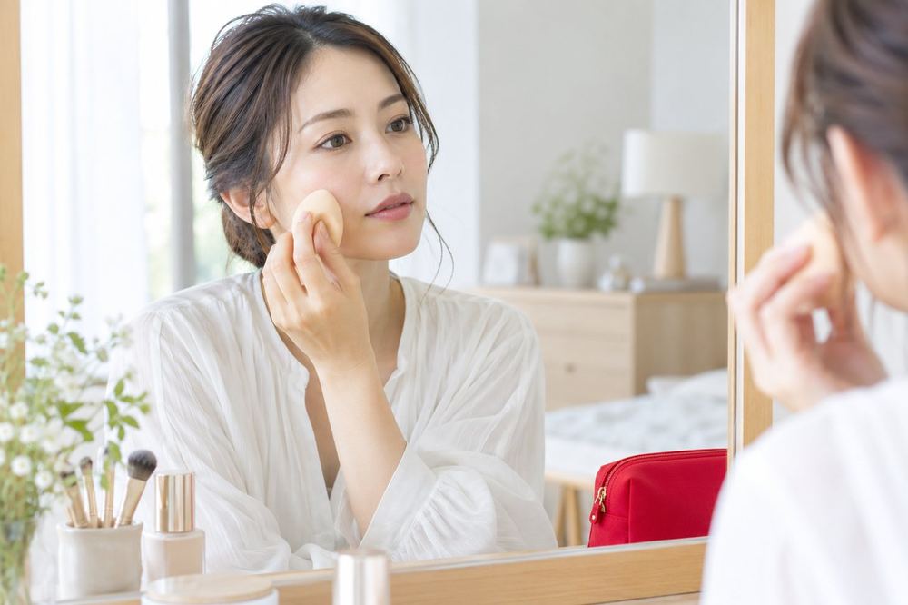 女性が鏡の前で、スポンジを使って頬のファンデーションをなじませている