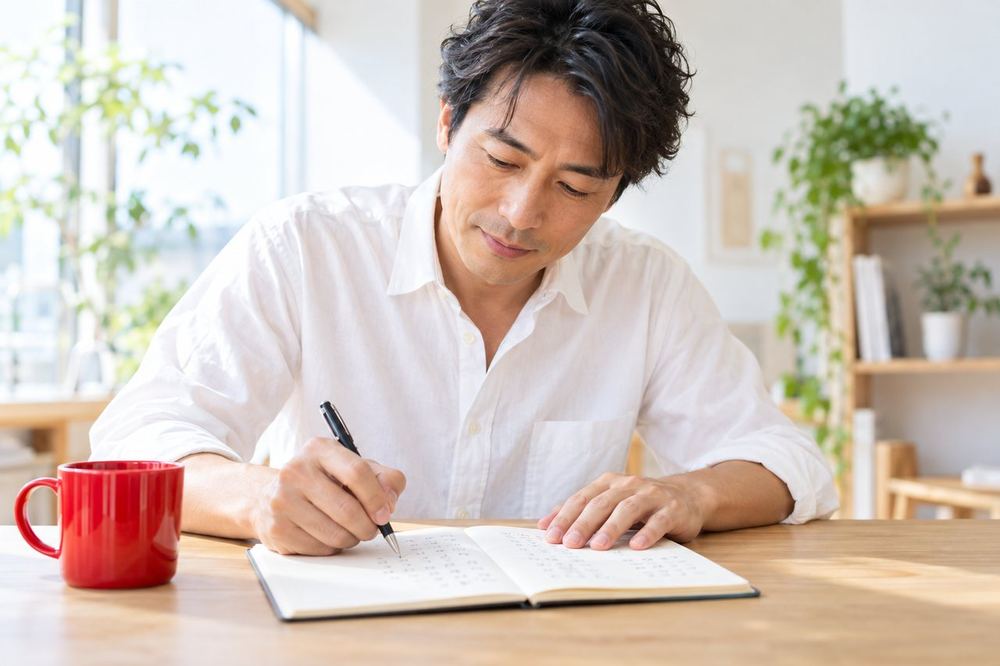 40代の男性が自宅の机でノートを開き、配信で話したいことと不安なことを二つの列に分けて書き出している