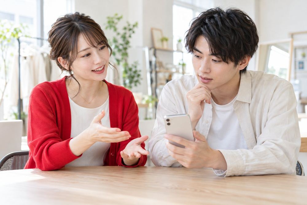 ライバー経験のある女性のマネージャーが、スマホを手にした20代の男性に初配信の準備を説明している
