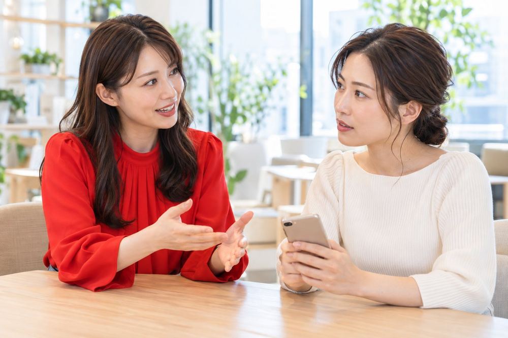 ライバー経験のある女性のマネージャーが、スマホを手にした30代の女性に、お金の手続きの相談先を説明している