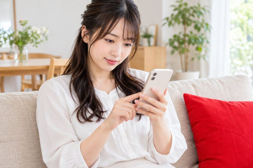 ソファに座った20代の女性が、スマホでLIVEの設定の画面を開き、コメントの設定を確かめている