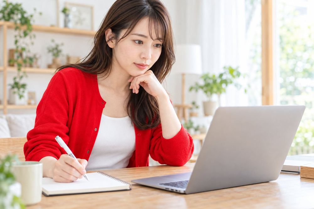 自宅の机でノートパソコンの請求書の画面を見ながら、手元のノートにメモを取っている20代の女性