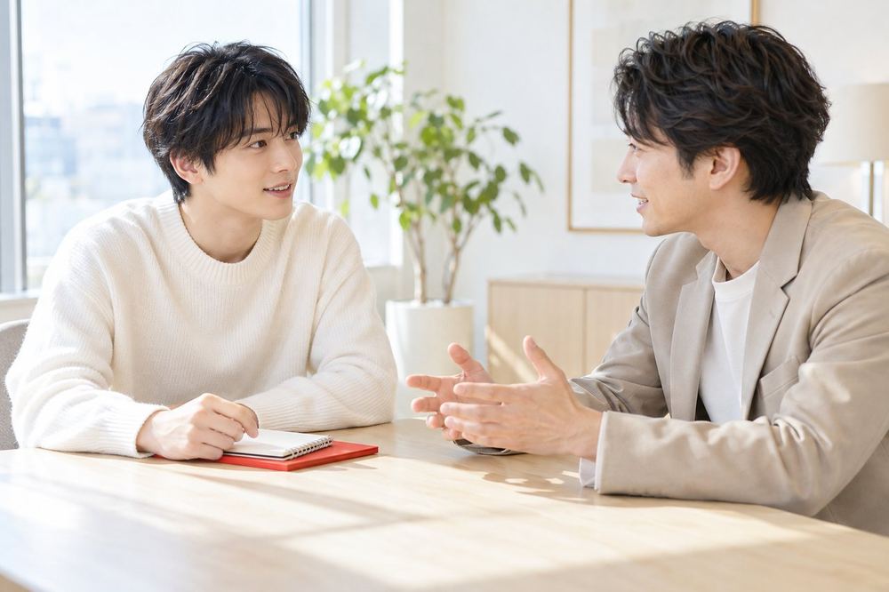 20代の男性が明るい会議室で、聞きたいことを書いたメモを手元に置き、事務所の担当者と向かい合って話している