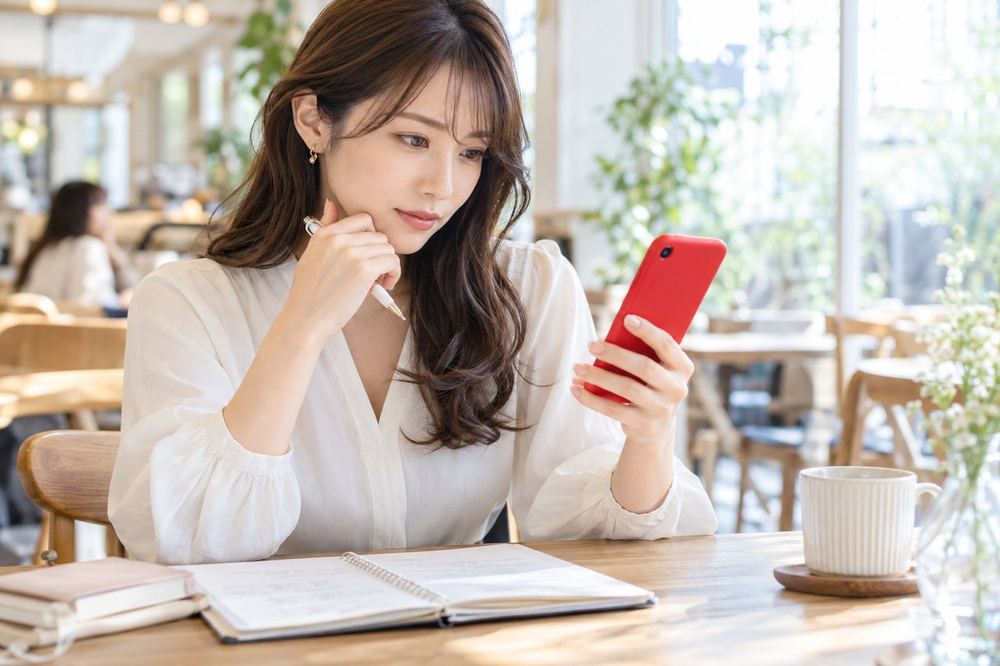 カフェで女性が面談の質問を書いたメモを広げ、スマホで確かめながら聞くことを整理している