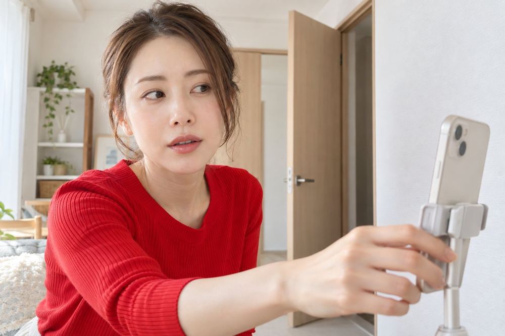 30代の女性が配信中、背後のドアが開いたことに気づき、落ち着いてスマホの向きを壁側に変えている