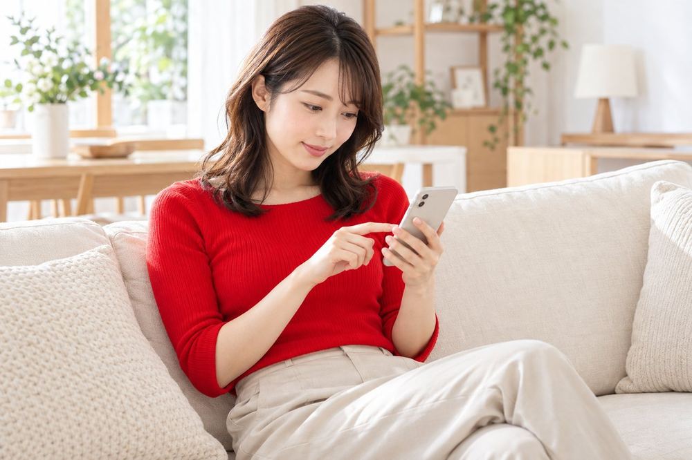 女性がソファでスマホのアプリ画面を開き、設定の項目を一つずつたどっている