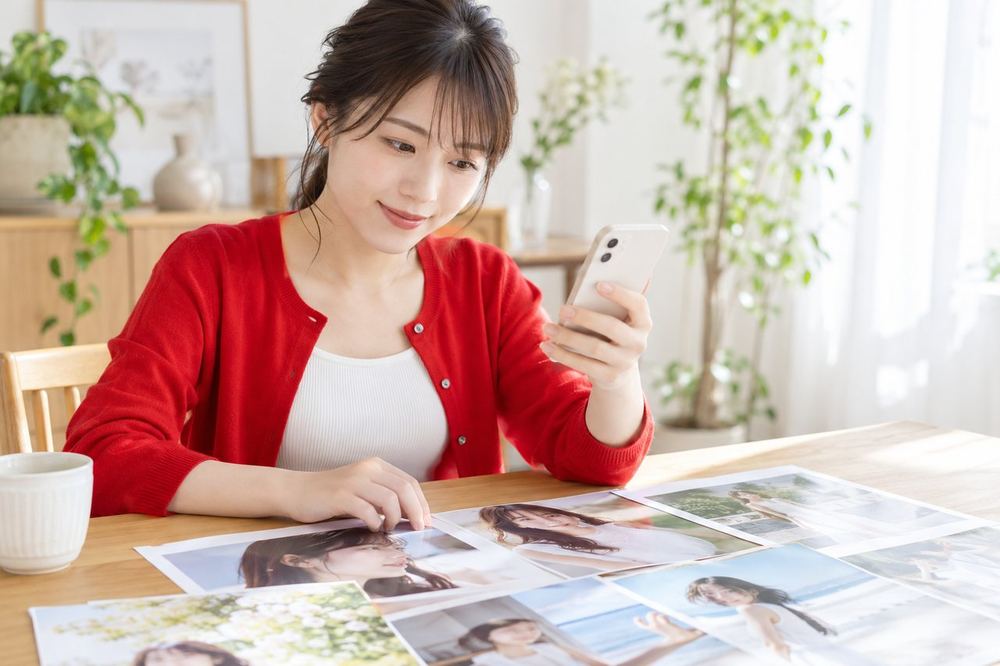 20代の女性が明るい部屋でスマホを見ながら、事務所についての資料をテーブルに広げて読んでいる