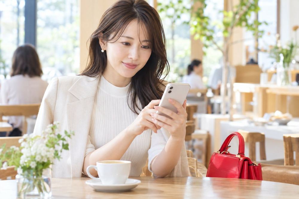 30代の女性がカフェの席でスマホを手に、落ち着いた表情で面談の予定を確認している