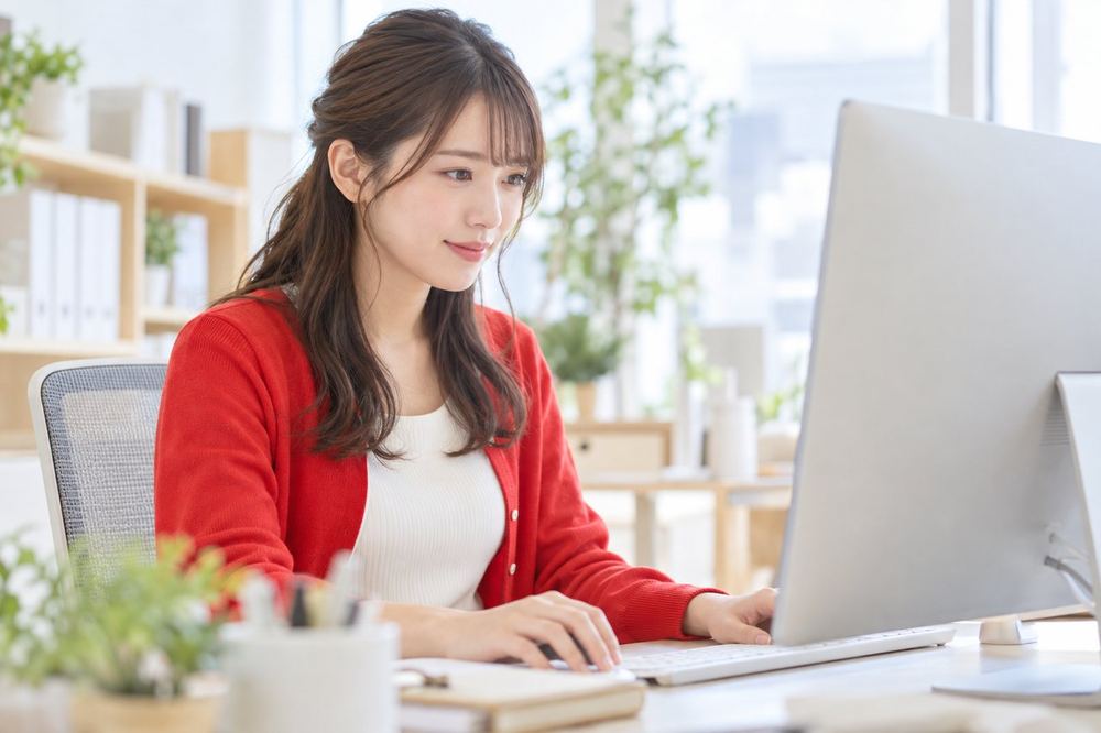 20代の女性スタッフがオフィスの席でパソコンの画面を見ながら、配信スケジュールの表を整理している