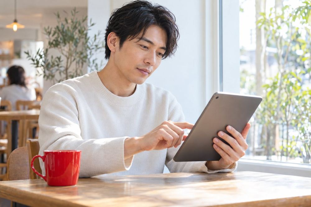 カフェの窓際で、30代の男性がタブレットに表示された公式の説明文を指でなぞりながら、重要な文に印をつけている