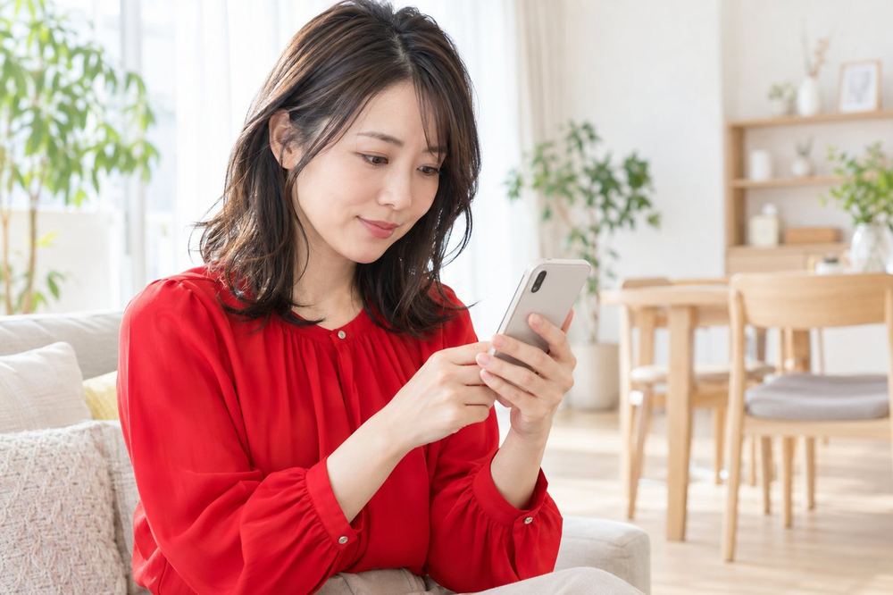 30代の女性がスマホを両手で持ち、画面下のメニューにライブの項目があるかを一つずつ確かめている