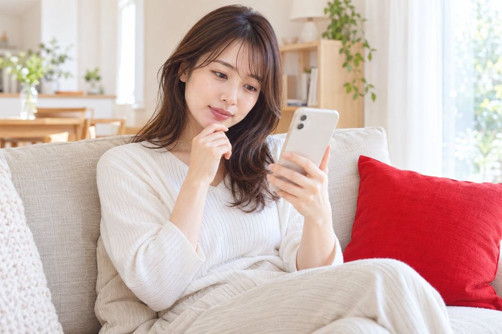 20代の女性がソファに座ってスマホで2人のライバーが並んで映る配信を見ながら、どういう仕組みなのか首をかしげている