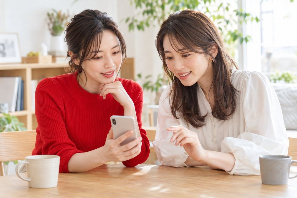 明るい部屋で、女性ふたりがスマホを見ながら、コラボやイベントへの出方を相談している