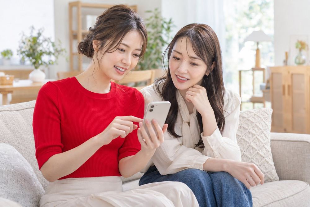 明るい部屋で、女性ふたりがソファに座り、スマホを見ながらコラボ配信の進め方を話し合っている