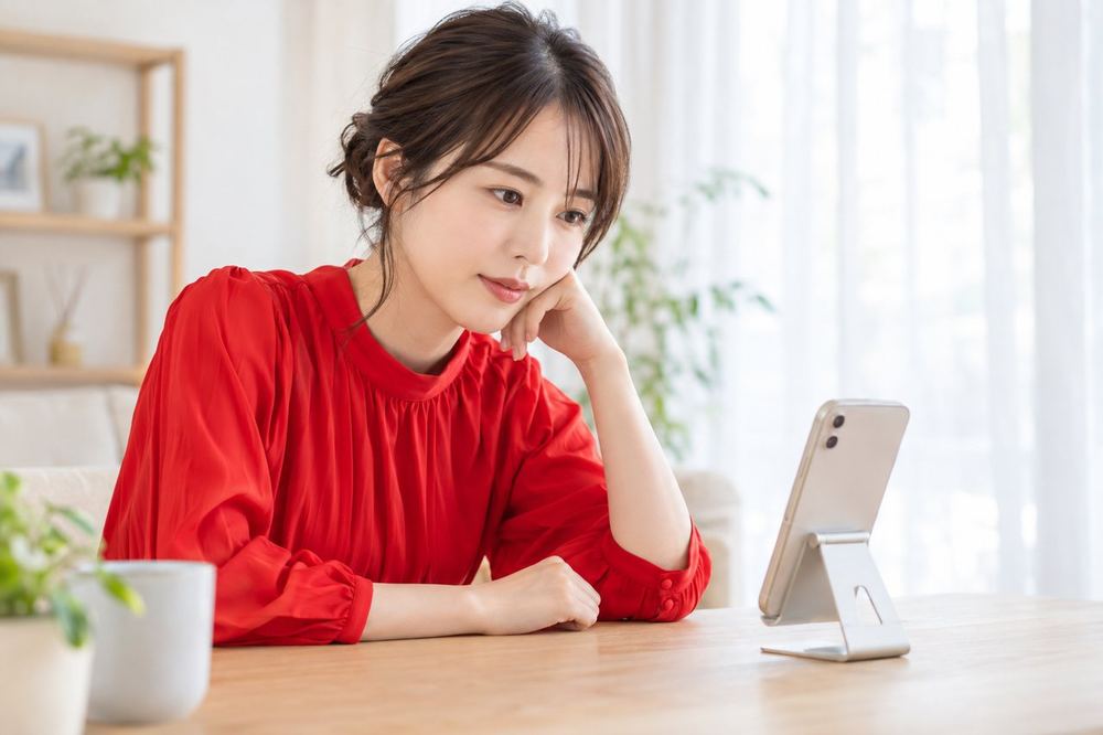 落ち着いた部屋で、女性が机のスマホを見ながら、配信のルールを確認している
