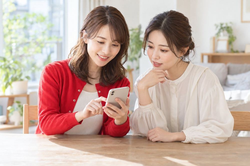 明るい部屋で、女性ふたりがスマホを見ながら、イベントや対戦への出方を相談している