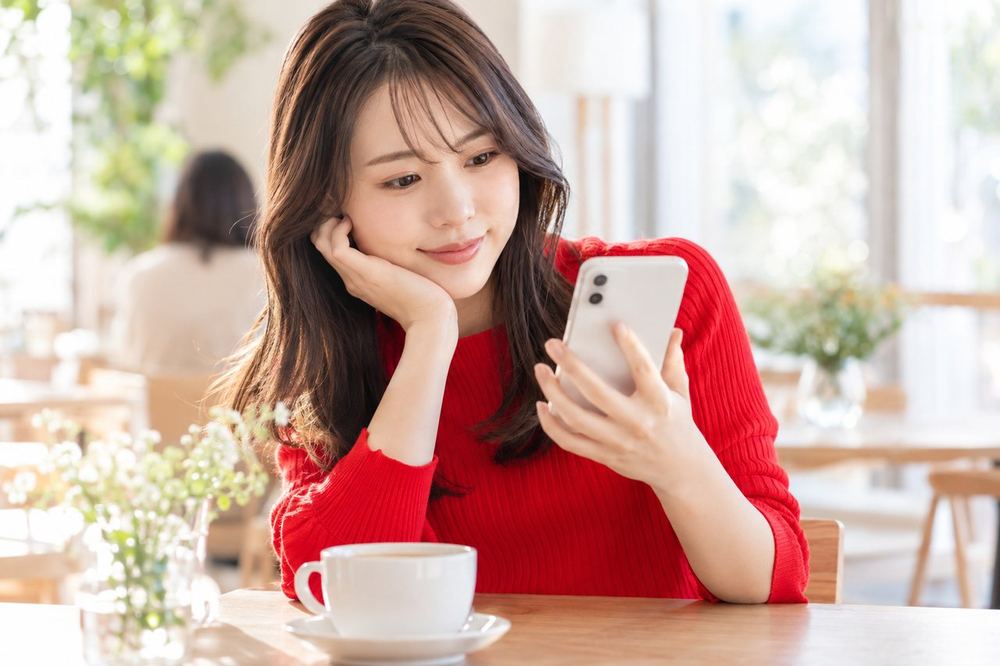 20代の女性がカフェの席でスマホのイベント一覧を見ながら、参加するかどうか考えている