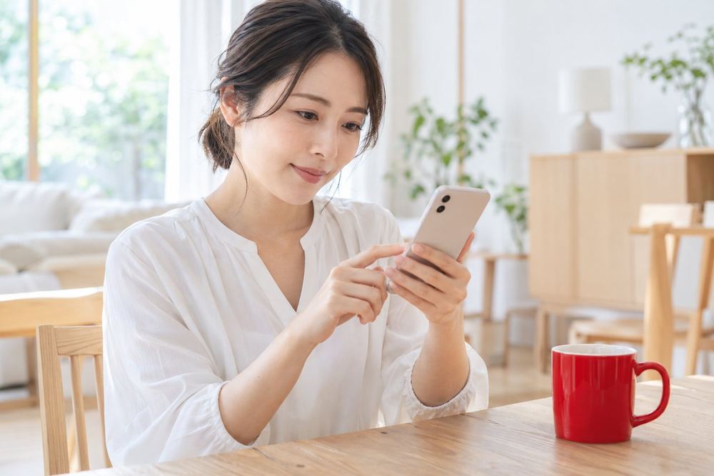 30代の女性がダイニングテーブルでスマホの設定画面を開き、自分の配信の条件を確かめている