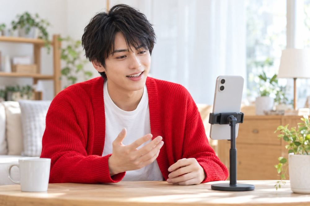 20代の男性がスマホに向かって笑顔で話しかけ、画面に出るコメントに目線を向けている