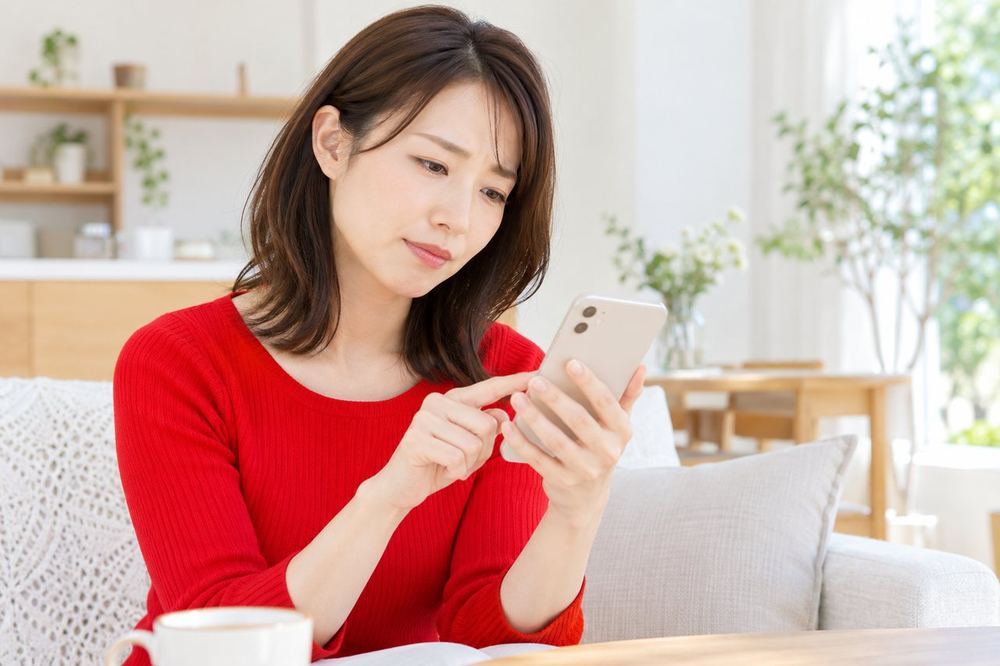 30代の女性がスマホの画面を見て首をかしげ、操作を確かめながらもう一度画面をたどっている