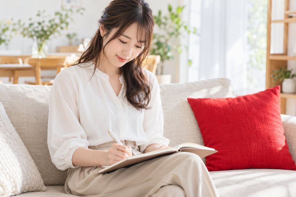 女性がソファでノートを広げ、配信した日時と気づいたことを一覧にして書き込んでいる