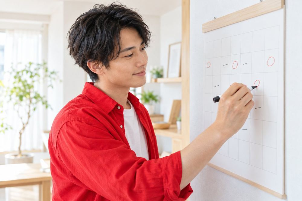男性が壁のカレンダーに配信の予定を書き込み、満足そうに確認している