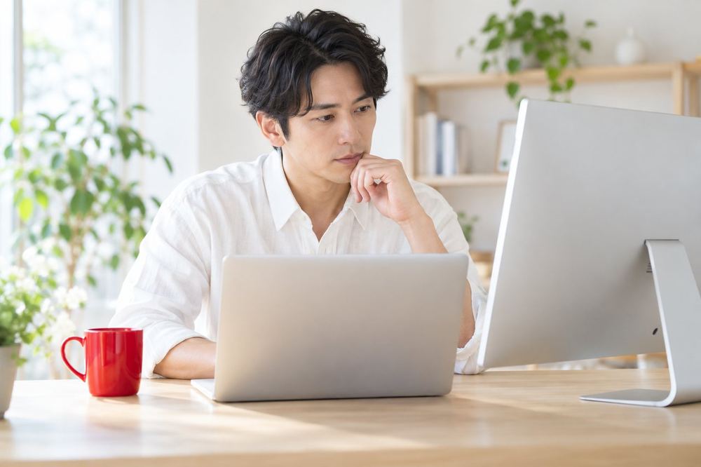 男性がノートパソコンを開き、見比べるように二つの画面を確認している