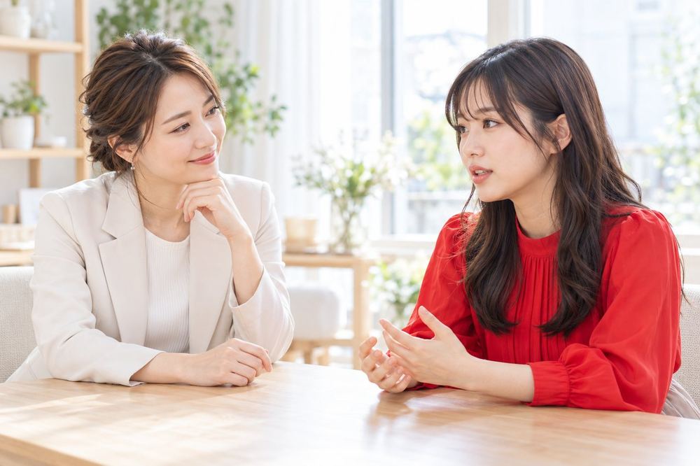明るい部屋でマネージャーの女性が、配信に悩む女性の話を笑顔でうなずきながら聞いている