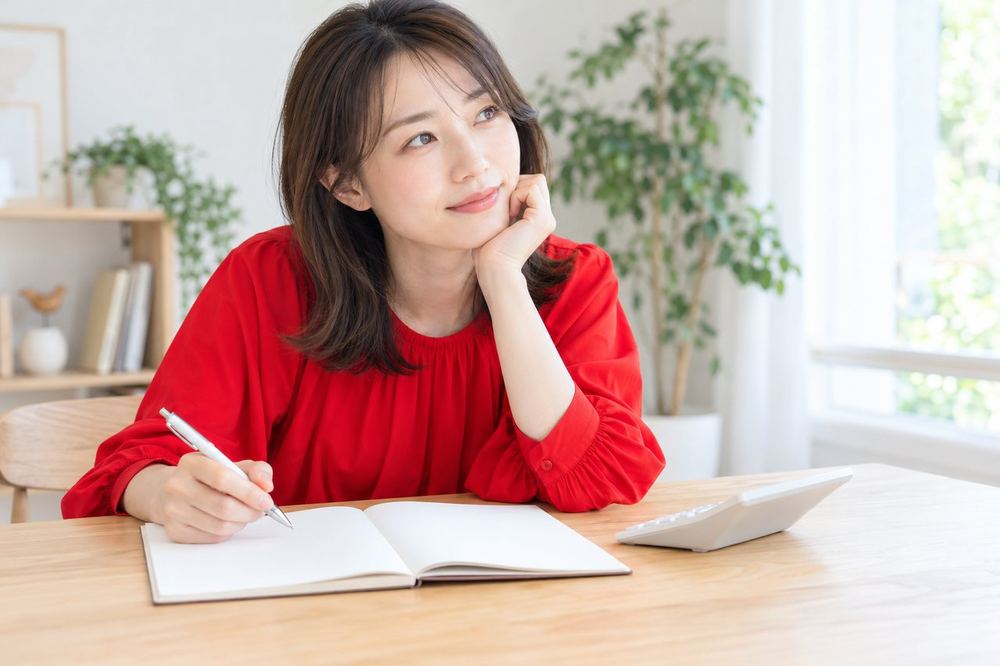 電卓とノートを机に置いて、副収入の記録のつけ方を考える女性