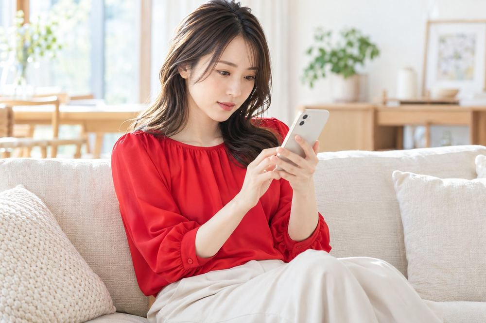 女性がソファに座って、スマホに届いた通知の画面を落ち着いて読んでいる