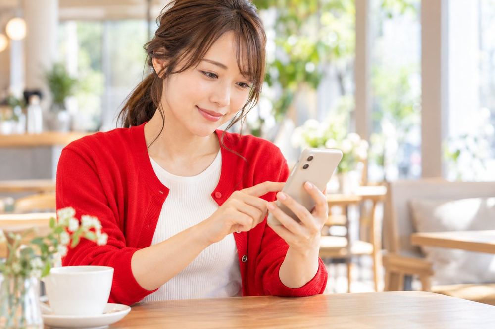 女性がカフェのテーブルでスマホを開き、次の配信の日時を入力している