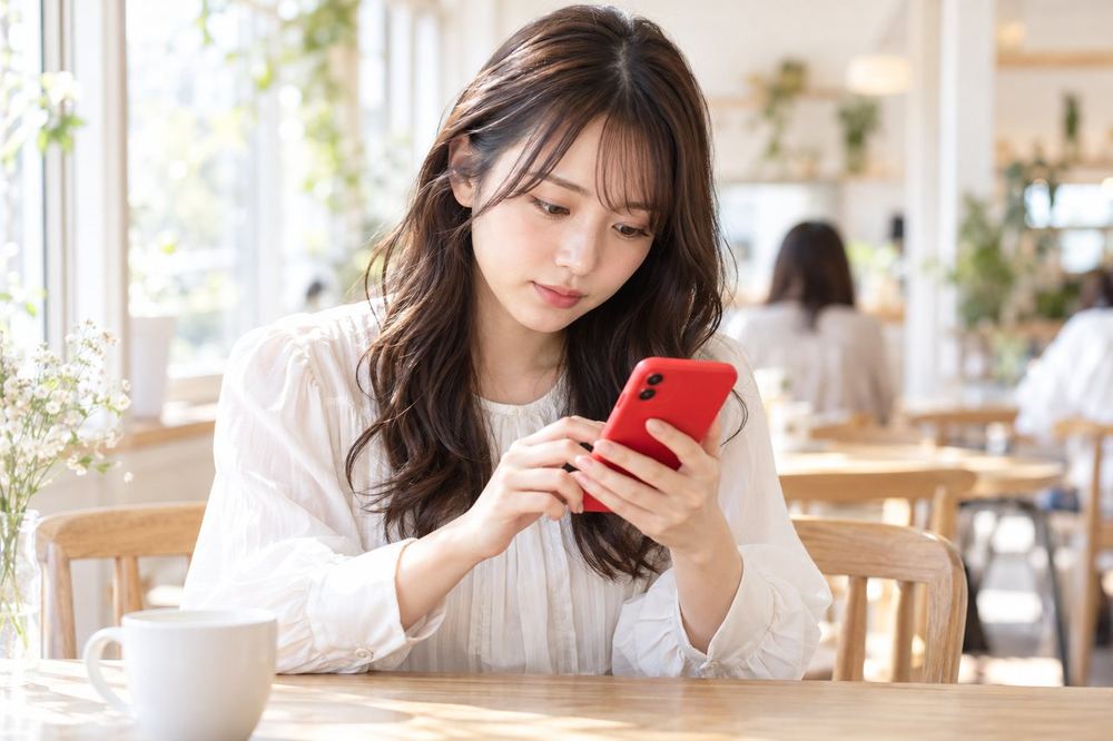 20代の女性がカフェの席で、スマホのメッセージ画面を見ながら配信の悩みを書き込んでいる