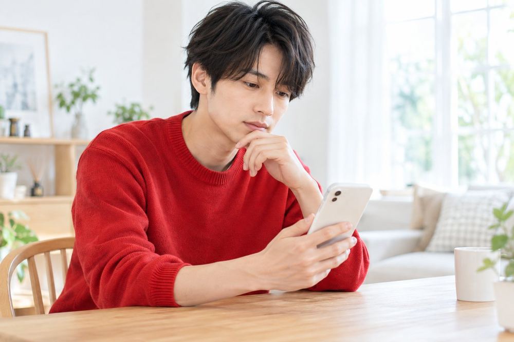 スマホの画面を見ながら、手を止めて慎重に考えている20代の男性