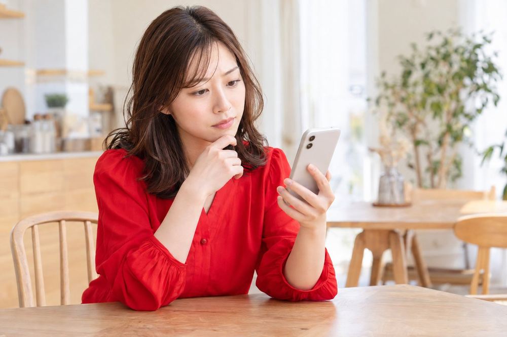女性がスマホを手に、プロモートの設定画面で予算の欄を見ながら考え込んでいる