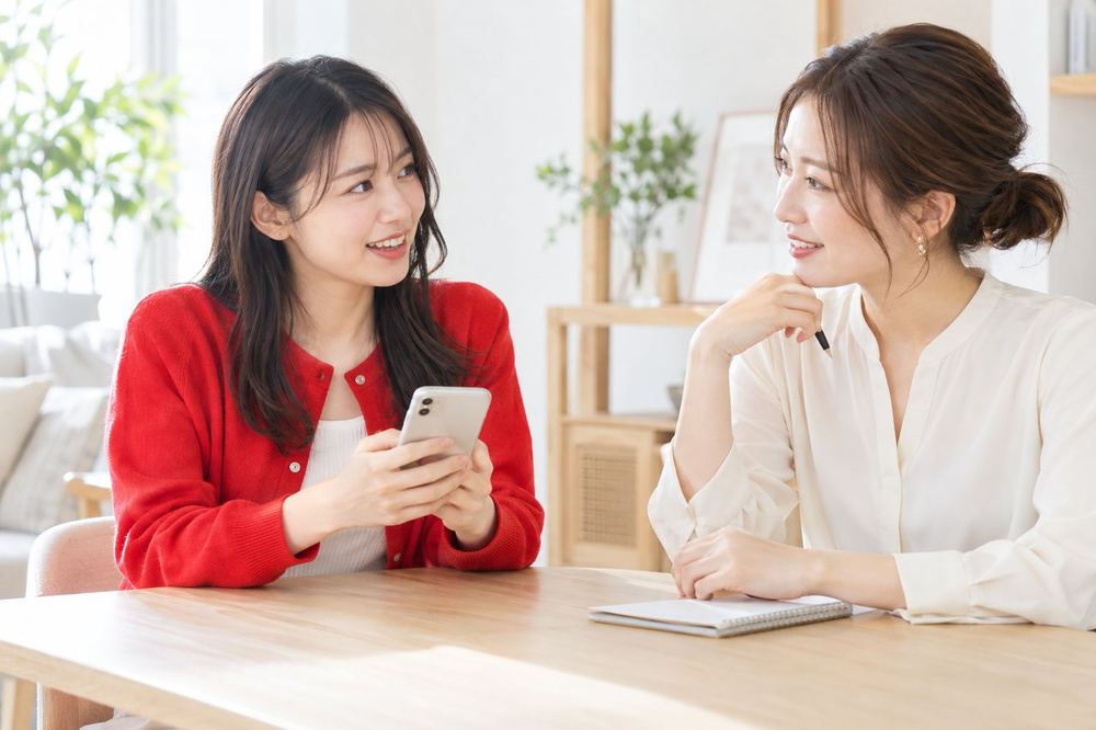 スマホを持った女性が、明るい部屋でマネージャーと向かい合って話している