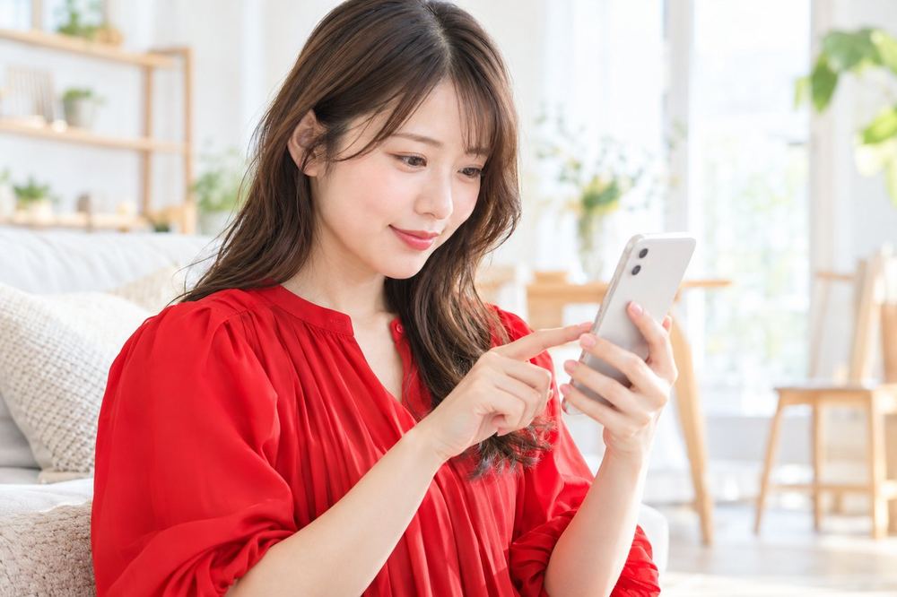 女性が明るい部屋で、スマホのLIVE画面に出ている順位の表示を、指でなぞりながら見比べている