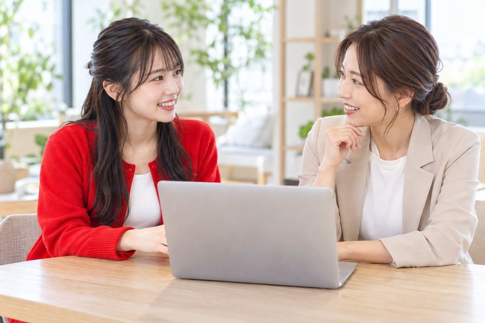 明るい打ち合わせスペースで、配信の振り返りについてマネージャーと話す20代の女性