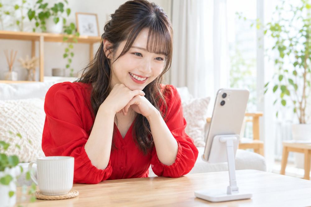 20代の女性がスマホで配信しながら、画面に届くギフトの通知を見て笑顔になっている