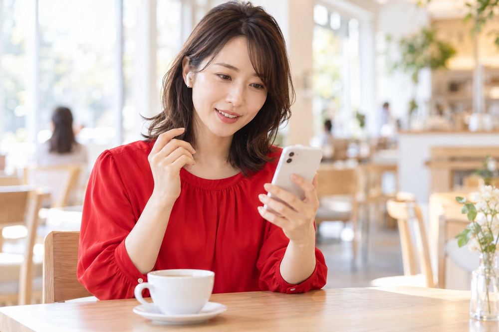 30代の女性がカフェでスマホの画面を見ながら、落ち着いた様子で電話で相談している