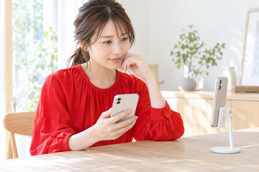 30代の女性がテーブルに置いたスマホの背面を見ながら、別のスマホで自分の配信画面を確かめている