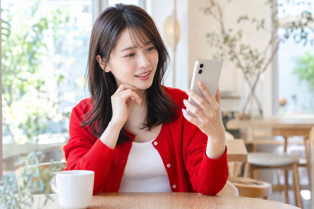 20代の女性がカフェでスマホを見ながら、落ち着いた表情でマネージャーとオンラインで話している