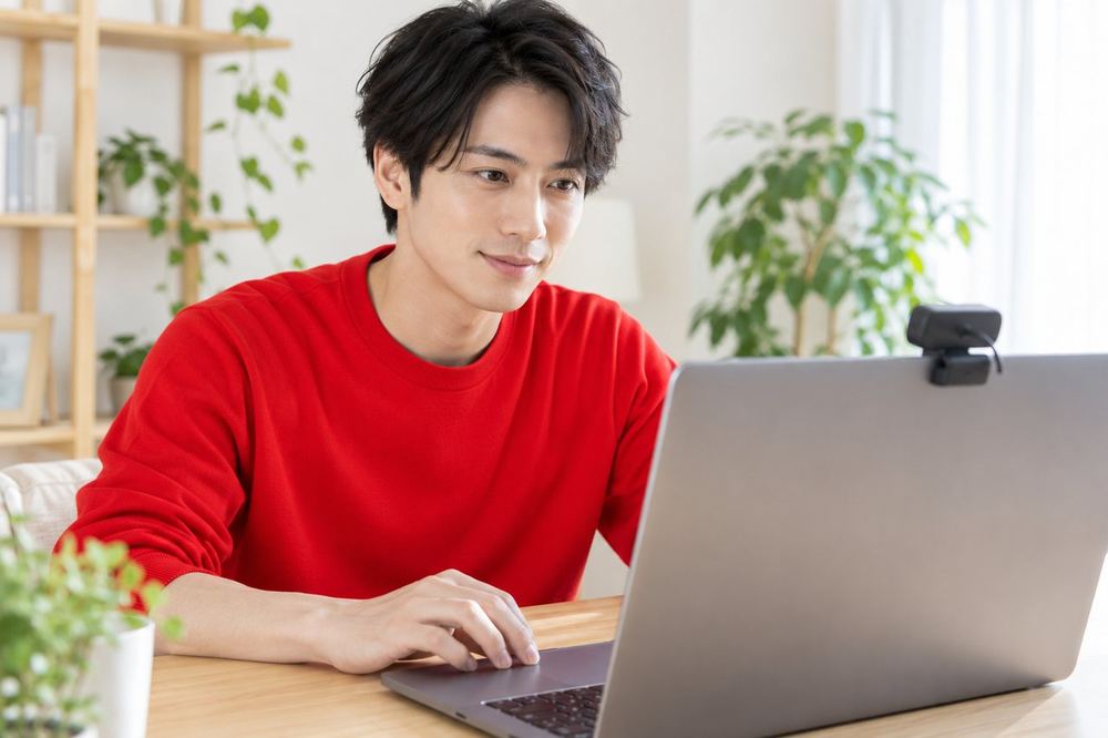 男性がデスクでノートパソコンとウェブカメラを使い、配信の設定を確認している