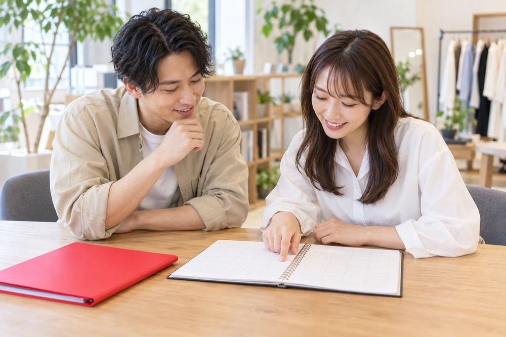 私服のマネージャーの男性が、テーブルで女性と配信の予定表を一緒に見ている