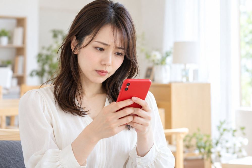 スマホでメッセージを読んでいる若い女性が、落ち着いて内容を確かめようと眉を寄せている
